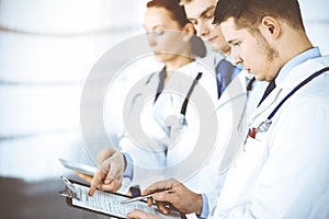 Doctors, two men and a woman, discussing medical exam resoults, while standing at sunny hospital office. Physicians use