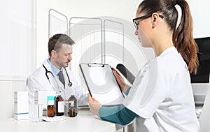 Doctors writing prescription at desk in medical office with drug