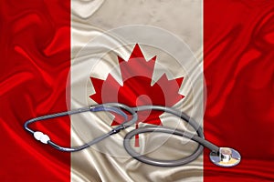 Doctorâ€™s tool, medical stethoscope, lies on the silk national flag of the state of Canada, the concept of tourism, insurance,