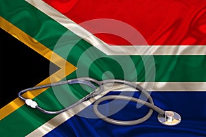 Doctorâ€™s tool, medical stethoscope, lies on the silk national flag of the state of South Africa, the concept of tourism,