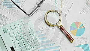 Documents with magnifying glass and calculator. Printed stock graphs and charts. Analyzing financial data report and