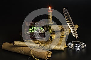 Documents in scrolls, a burning candle, an old book, a chest with jewelry on a black background