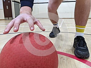 Dodgeball player picking up a large red dodge ball in a sportshall