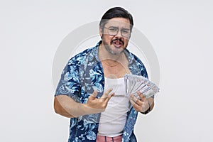 Dodgy and sleazy middle-aged man in a Hawaiian shirt pompously showing off a wad of cash, portraying wealth, standing isolated on