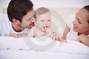 She does the cutest things. Two loving young parents and their adorable baby daughter lying together on a bed.