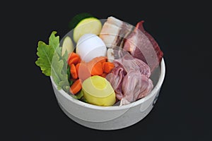 Dog bowl filled with mixture of biologically appropriate raw food containing meat chunks, vegetables, potato, egg