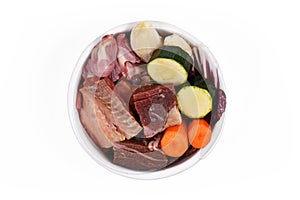 Dog bowl with species appropriated raw food like chunks of raw meat, fish, chicken stomache and vegetabls like carrots