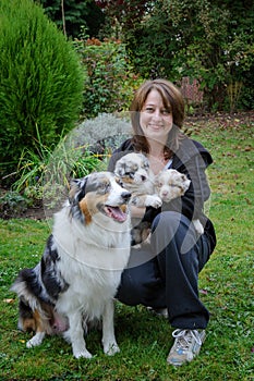 Dog breeder with Australian Shepherd adult female dog and her puppies in arms