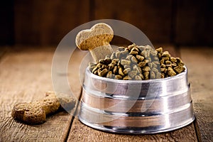 Dog food with bone shaped dog biscuit in metallic bowl on wooden background, copy space