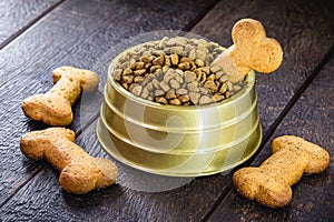 Dog food with bone shaped dog biscuit in metallic bowl on wooden background, copy space