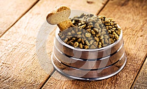 Dog food with bone shaped dog biscuit in metallic bowl on wooden background, copy space