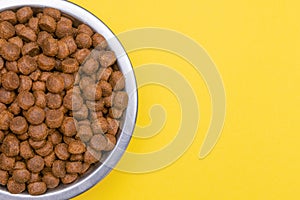 Dog food in a Half silver bowl. Left side. Yellow background. Copy, text sapce