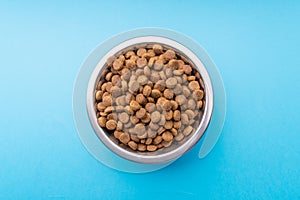 Dog food in a metal bowl. Blue background. From above