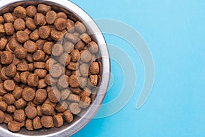 Dog food in a silver bowl. Half of the bowl on the left. Blue background. Copy, text sapce