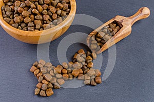 Dog food in a wooden bowl with a scoop on black background