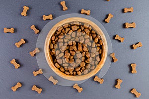 Dog food in a wooden bowl and snack like bones on black background, flat lay