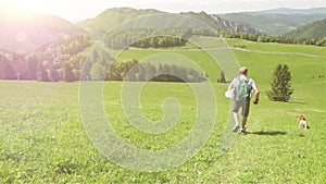 A dog with its master running down the green hill while mountaineering