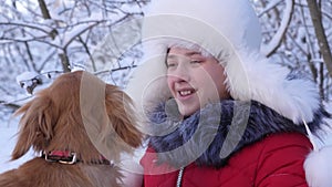 Dog kisses the hostess. dog licks girl`s face. Beautiful girl smiles, caresses her beloved dog in winter in park. girl