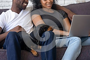 Dog lays down on black family knees looking at laptop