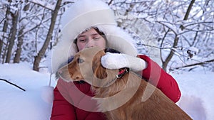 Dog licks girl`s face. Beautiful girl smiles, caresses her beloved dog in winter in park. girl with hunting dog walks in