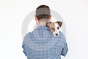 The dog lies on the shoulder of its owner. Jack Russell Terrier in his owner`s hands on white background. The concept of people an