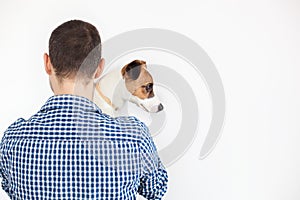 The dog lies on the shoulder of its owner. Jack Russell Terrier in his owner`s hands on white background. The concept of people an