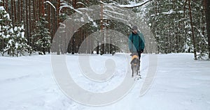 the dog in an orange blanket runs to his master along a path in a winter forest