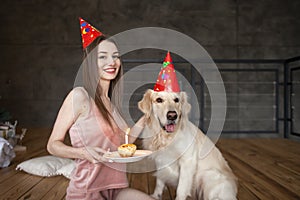 dog's birthday, young woman with golden retriever in festive hats celebrates birthday, girl congratulates her pet