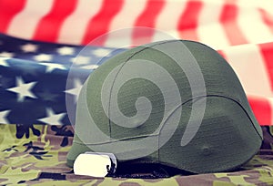 Dog tags and helmet on camouflage fabric in the background American flag.