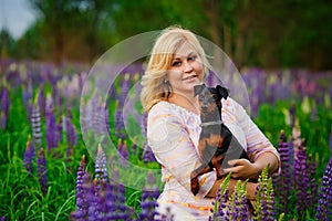 Dog and women concept - . A young plump blonde woman hugs and kisses her beautiful black dog in a pink and purple flower field