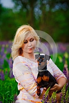 Dog and women concept - . A young plump blonde woman hugs and kisses her beautiful black dog in a pink and purple flower field