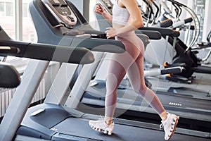 Doing cardio by running on the racetrack. Young beautiful woman in sportive clothes have fitness day in the gym