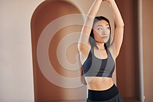 Doing fitness exercises. Young serious asian woman standing indoors