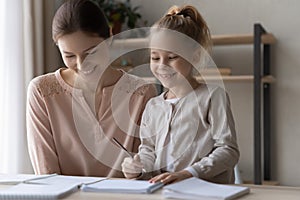 Happy preteen girl preparing school assignment with help of mother photo