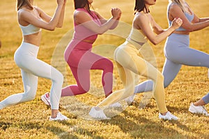 Doing legs exercises. Group of women have fitness outdoors on the field together