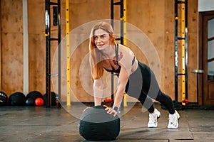 Doing push ups by using soft ball. Beautiful strong woman is in the gym