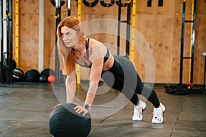 Doing push ups by using soft ball. Beautiful strong woman is in the gym