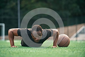 Doing push ups. Young black man is with basketball ball outdoors