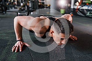 Doing push-ups. Young sportive strong man in black wear have workout day in gym