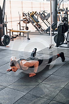 Doing push-ups. Young sportive strong man in black wear have workout day in gym