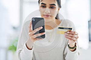 Doing some shopping from the business budget. a young businesswoman using a cellphone and credit card in an office.