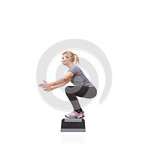Doing squats to tone her body. A smiling young woman doing aerobics on an aerobic step against a white background.