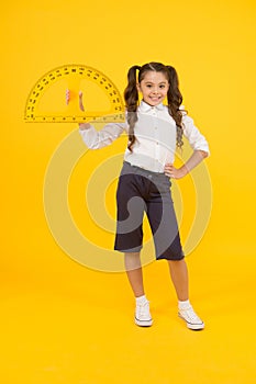 Doing well at maths. Cute little schoolgirl holding measuring tool for maths on yellow background. Small child with