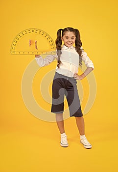 Doing well at maths. Cute little schoolgirl holding measuring tool for maths on yellow background. Small child with