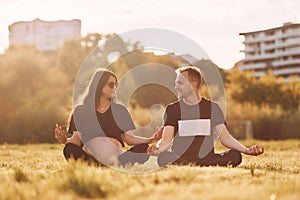 Doing yoga. Woman is pregnant. Lovely couple sitting on the field together