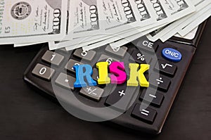 Dolars and the word `risk` from the letters lies on the calculator. Close-up. The concept of business risk, economic crisis.