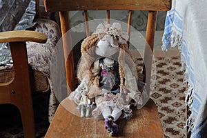 The doll in a beautiful dress sits on a wooden chair