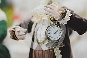 The doll is holding an old mechanical watch with a flip cover