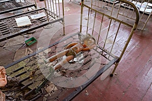 Doll on metal grid of bed in abandoned kindergarten in destroyed village Kopachi Chernobyl NPP alienation zone, Ukraine photo