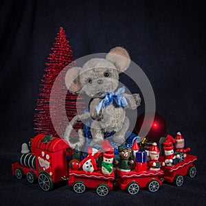 A doll mouse on a chair, next to a Christmas tree and a toy locomotive with wagons